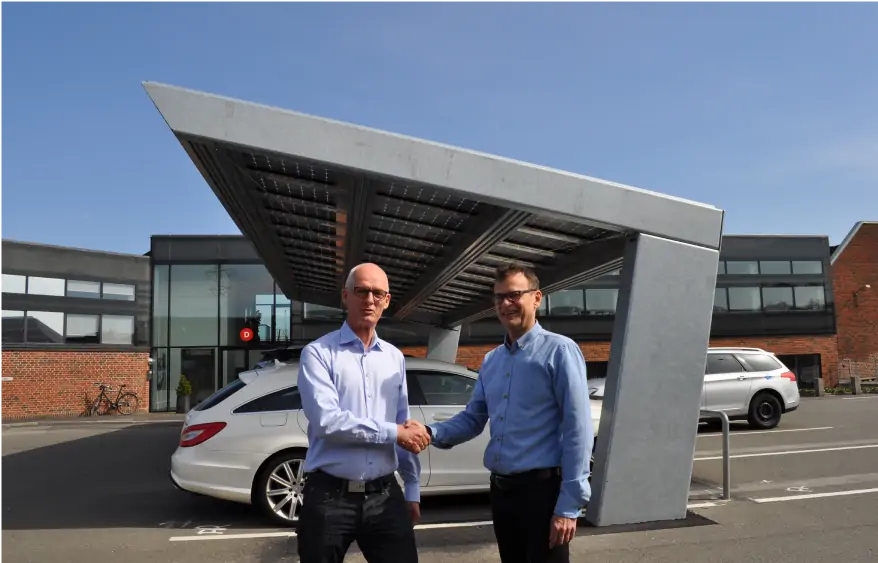 Two men in front of solar carport featuring energy-efficient panels, providing shade and renewable energy in a parking lot, showcasing innovative solar power solutions.